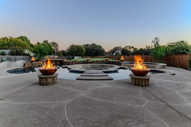 patio terrace at dusk featuring a fire pit and a swimming pool with hot tub