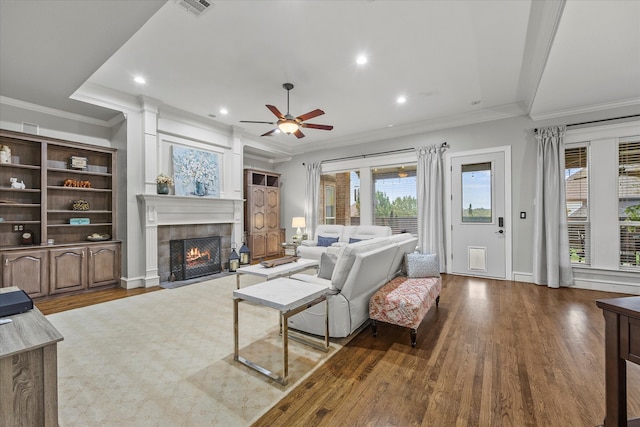 living room with ornamental molding, wood-type flooring, ceiling fan, and a tile fireplace