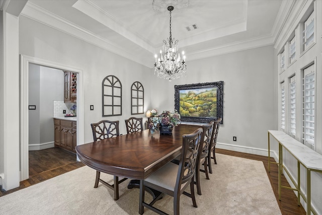 dining area featuring dark hardwood / wood-style floors, a raised ceiling, an inviting chandelier, and crown molding