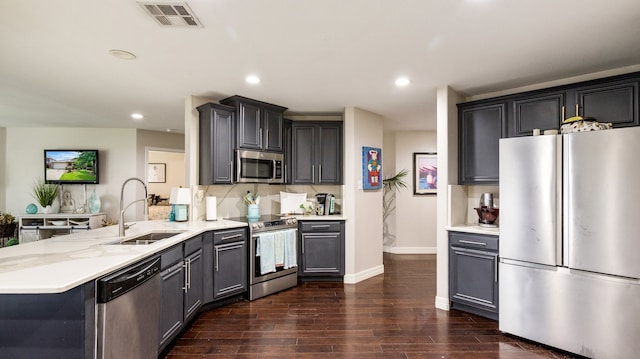 kitchen featuring sink, light stone counters, kitchen peninsula, appliances with stainless steel finishes, and dark wood-type flooring