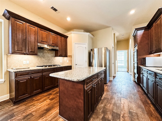 kitchen featuring appliances with stainless steel finishes, light stone counters, tasteful backsplash, a center island, and dark hardwood / wood-style flooring