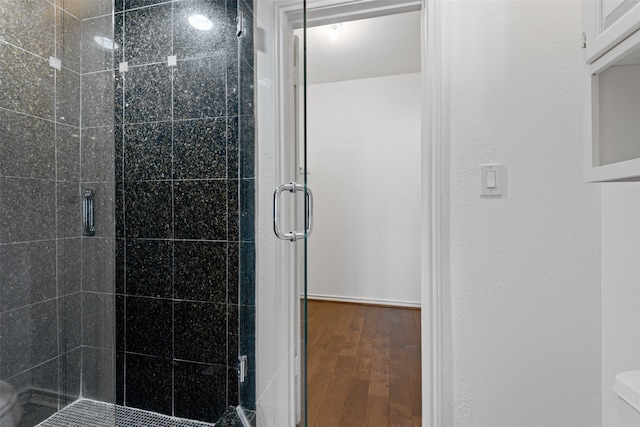 bathroom featuring wood-type flooring, toilet, and a shower with shower door