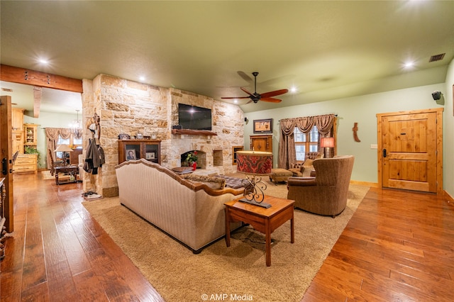 living room featuring a stone fireplace, hardwood / wood-style floors, and ceiling fan with notable chandelier