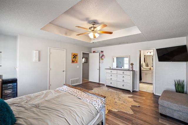 bedroom featuring ensuite bath, wood-type flooring, ceiling fan, and a raised ceiling