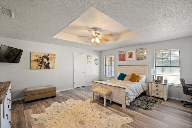 bedroom with hardwood / wood-style flooring, ceiling fan, a textured ceiling, and a tray ceiling