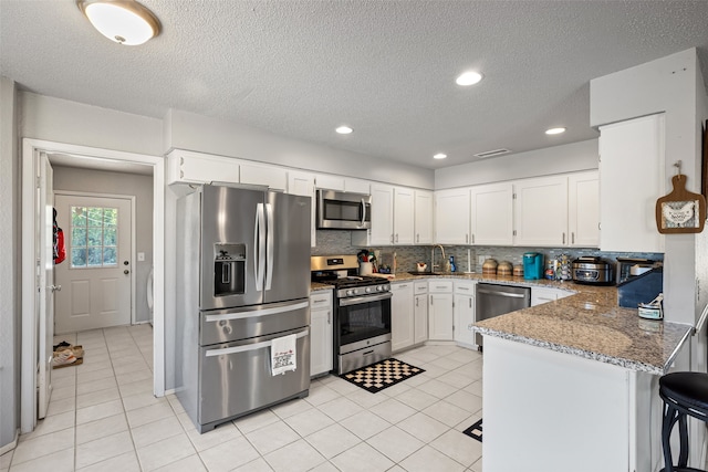 kitchen with stainless steel appliances, white cabinets, kitchen peninsula, backsplash, and light stone countertops