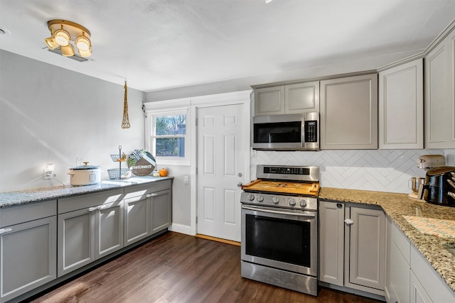 kitchen with gray cabinets, appliances with stainless steel finishes, light stone countertops, and dark hardwood / wood-style flooring