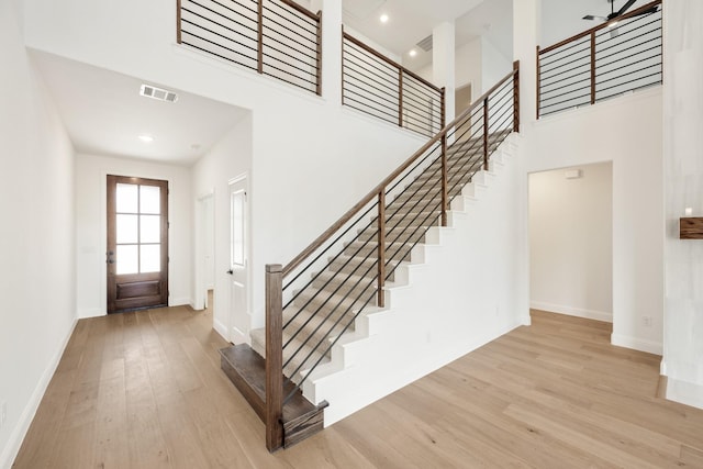 entryway with a towering ceiling, wood finished floors, visible vents, and baseboards