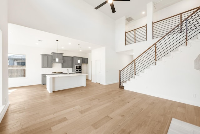 unfurnished living room with baseboards, visible vents, a ceiling fan, stairs, and light wood-style floors