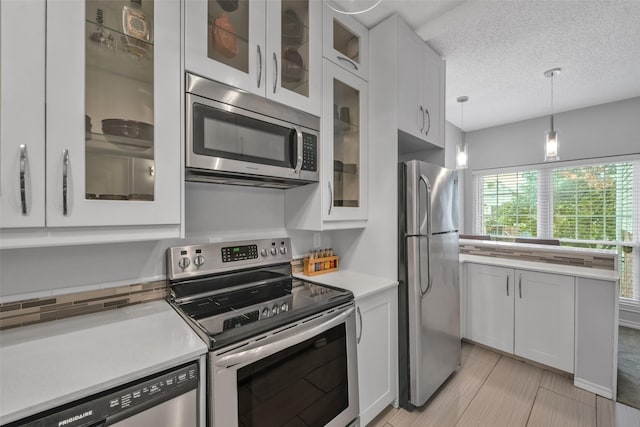 kitchen featuring a textured ceiling, appliances with stainless steel finishes, decorative light fixtures, light tile patterned flooring, and white cabinetry