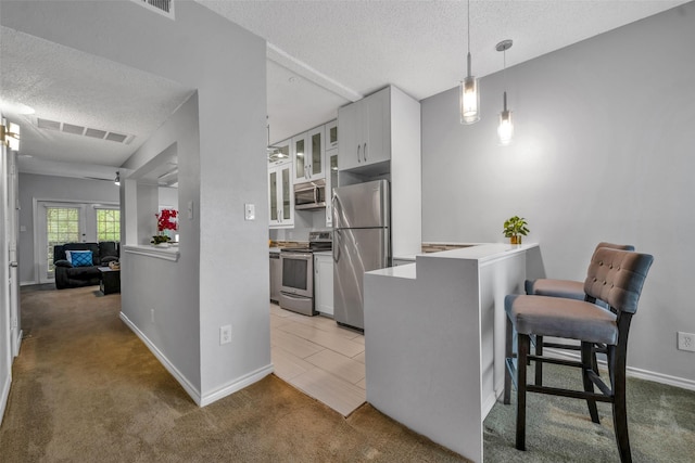 kitchen featuring white cabinetry, hanging light fixtures, carpet floors, a textured ceiling, and appliances with stainless steel finishes