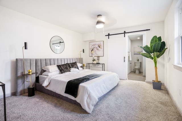 carpeted bedroom with a barn door, ensuite bath, and ceiling fan