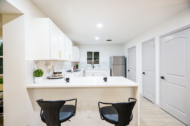 kitchen with white cabinets, decorative backsplash, kitchen peninsula, a breakfast bar area, and stainless steel refrigerator