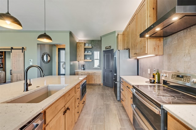 kitchen with stainless steel appliances, wall chimney range hood, decorative light fixtures, a barn door, and sink