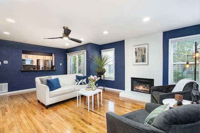 living room with a fireplace, light hardwood / wood-style floors, and ceiling fan