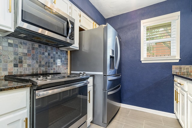 kitchen featuring white cabinets, backsplash, appliances with stainless steel finishes, and dark stone counters