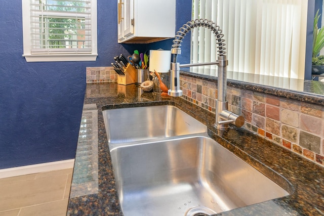 interior details with white cabinets, backsplash, sink, and dark stone counters