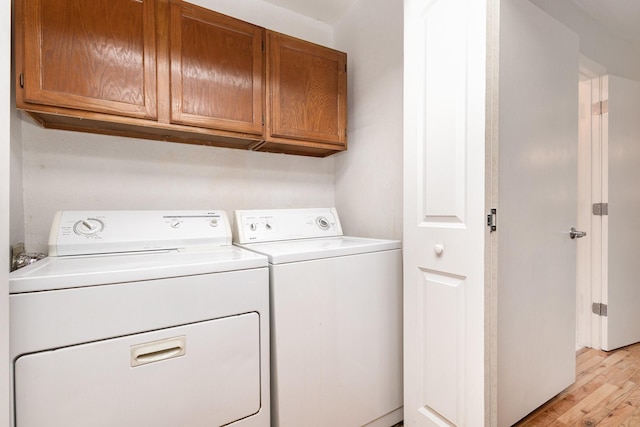 clothes washing area featuring washing machine and clothes dryer, light hardwood / wood-style flooring, and cabinets