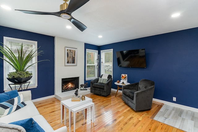 living room featuring ceiling fan, a healthy amount of sunlight, wood-type flooring, and a brick fireplace