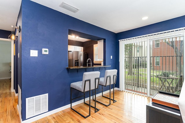 kitchen with a breakfast bar, sink, stainless steel refrigerator with ice dispenser, light wood-type flooring, and kitchen peninsula