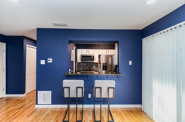 kitchen featuring decorative backsplash, light wood-type flooring, appliances with stainless steel finishes, a kitchen bar, and kitchen peninsula