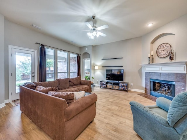 living room featuring light wood-type flooring, ceiling fan, and a tiled fireplace