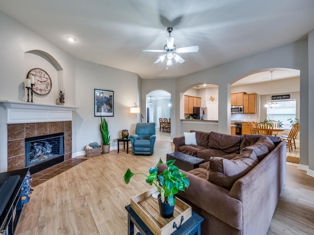 living room with light wood-type flooring, ceiling fan, and a tiled fireplace