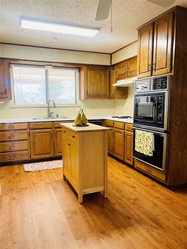 kitchen featuring a textured ceiling, sink, a kitchen island, double oven, and light hardwood / wood-style flooring