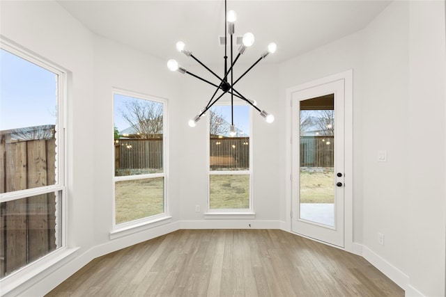 unfurnished dining area featuring an inviting chandelier, baseboards, and wood finished floors