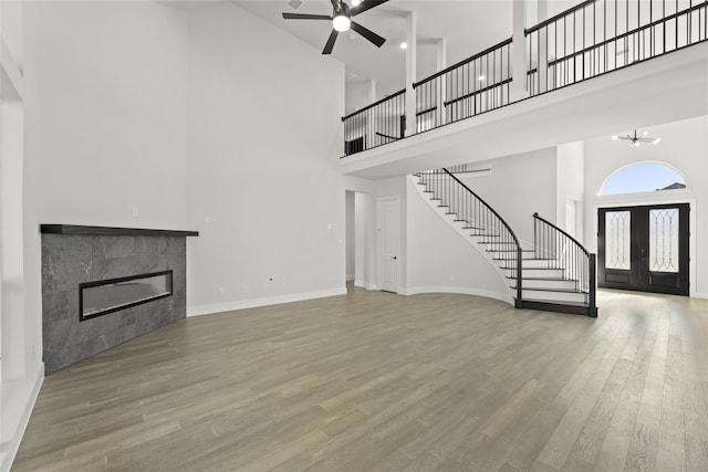 unfurnished living room with wood-type flooring, ceiling fan with notable chandelier, a tiled fireplace, and a high ceiling