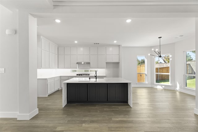 kitchen featuring a wealth of natural light, hardwood / wood-style floors, an island with sink, a chandelier, and white cabinets