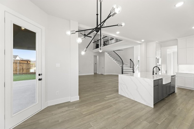 kitchen featuring light stone counters, a kitchen island with sink, white cabinets, built in microwave, and light wood finished floors