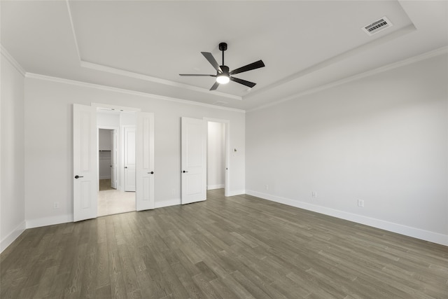 unfurnished bedroom with ceiling fan, dark hardwood / wood-style floors, a raised ceiling, and ornamental molding