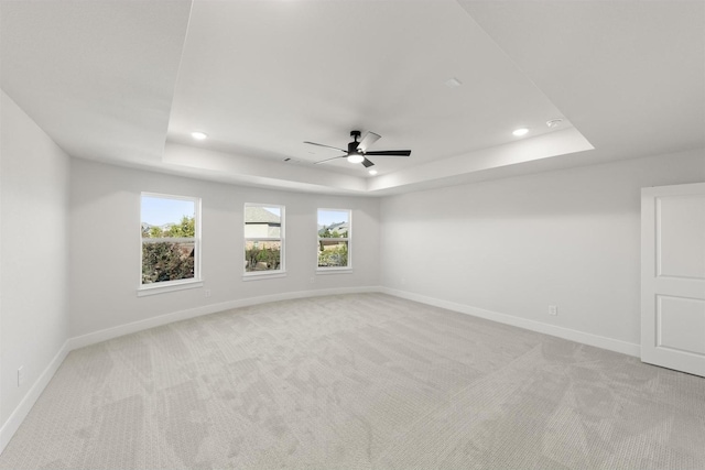 empty room featuring a raised ceiling, light colored carpet, and baseboards