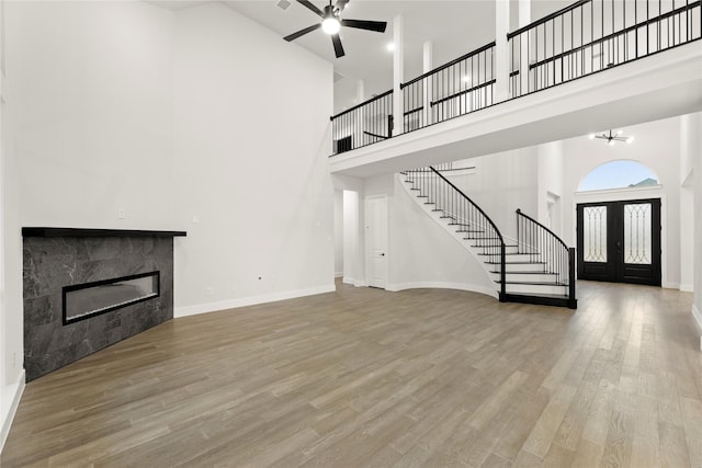 unfurnished living room featuring french doors, a fireplace, stairway, wood finished floors, and baseboards