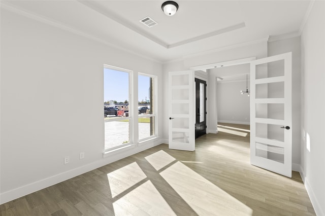 unfurnished room with french doors, ornamental molding, a raised ceiling, wood-type flooring, and a chandelier