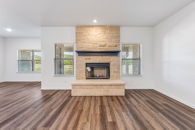 unfurnished living room featuring a stone fireplace, baseboards, and dark wood finished floors