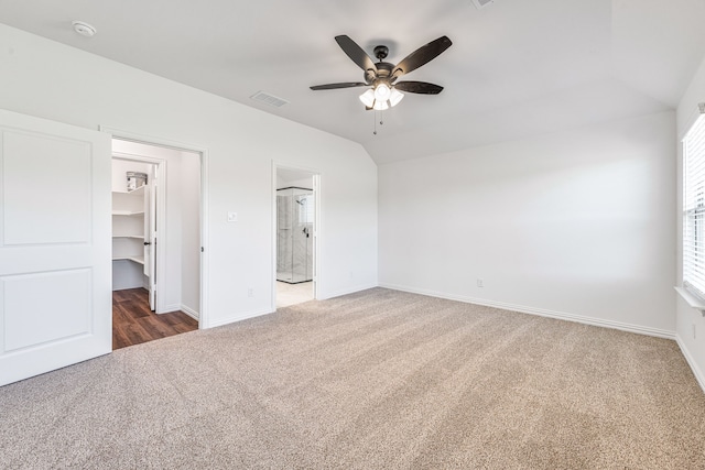 unfurnished bedroom featuring lofted ceiling, visible vents, a walk in closet, carpet floors, and baseboards