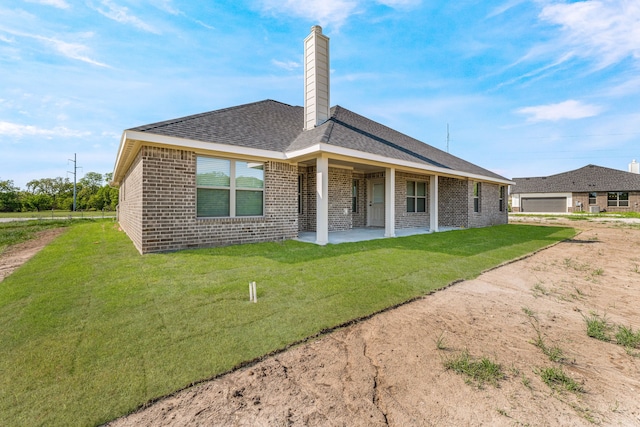 rear view of property featuring a chimney, a lawn, a patio, a garage, and brick siding