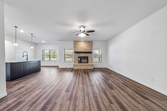 unfurnished living room with ceiling fan, baseboards, a healthy amount of sunlight, and dark wood-type flooring