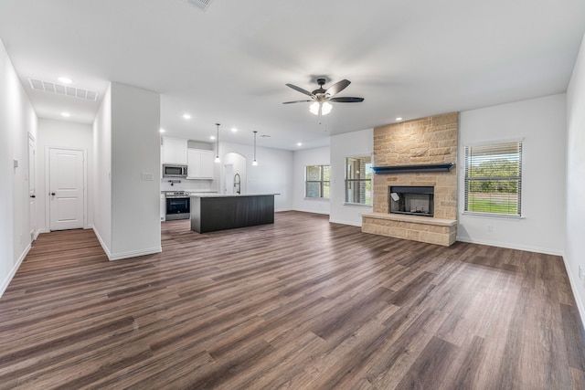 unfurnished living room featuring plenty of natural light, visible vents, dark wood-type flooring, and ceiling fan
