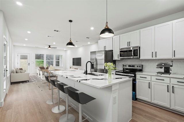 kitchen with white cabinetry, sink, appliances with stainless steel finishes, hanging light fixtures, and an island with sink