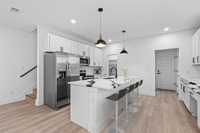 kitchen with a center island with sink, stainless steel appliances, white cabinetry, light stone countertops, and light hardwood / wood-style flooring