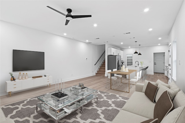 living room with light wood-type flooring, ceiling fan, and sink