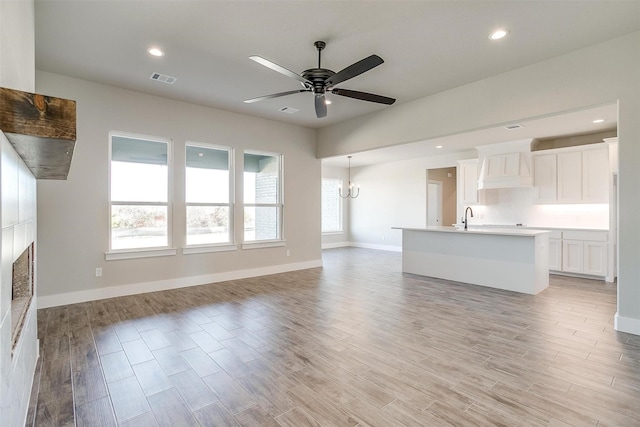 unfurnished living room with ceiling fan with notable chandelier, light hardwood / wood-style floors, and sink