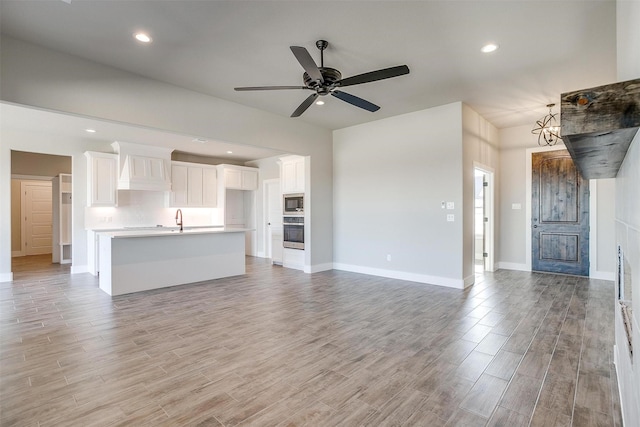 unfurnished living room featuring ceiling fan with notable chandelier, light hardwood / wood-style floors, and sink