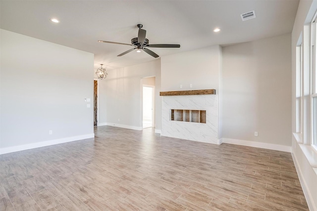 unfurnished living room with hardwood / wood-style floors, ceiling fan with notable chandelier, and a premium fireplace