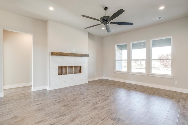 unfurnished living room with ceiling fan, light wood-type flooring, and a tiled fireplace