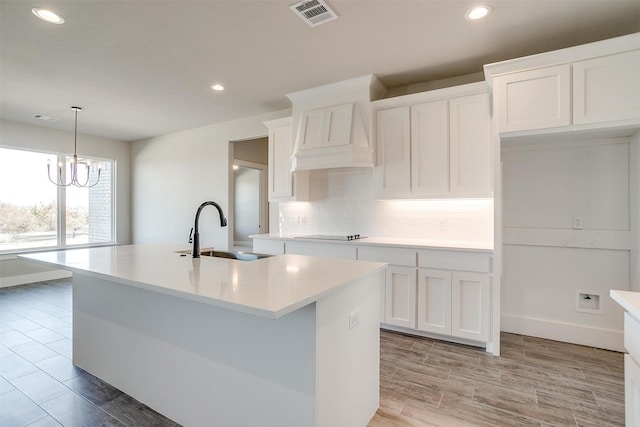 kitchen with sink, white cabinets, a chandelier, and a center island with sink