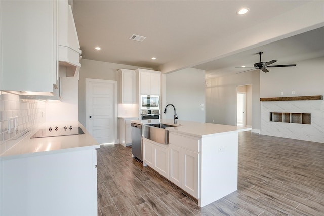 kitchen featuring stainless steel appliances, sink, white cabinets, light hardwood / wood-style floors, and an island with sink